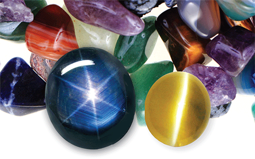 L to R: Blue sapphire with asterism; yellow topaz with chatoyancy against background of assorted gemstones.